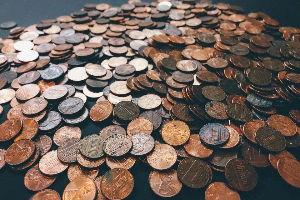 A large pile of scattered pennies and other small coins on a dark surface.