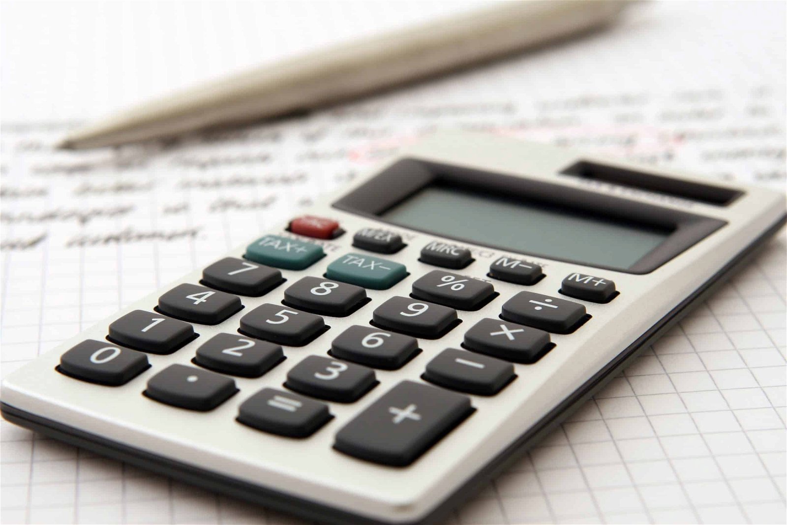 A close-up image of a calculator atop a sheet of graph paper with a pencil lying beside it, emphasizing the calculation of employee turnover rate.