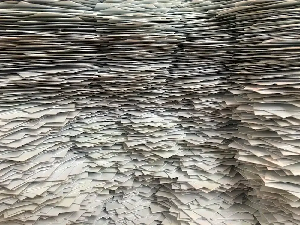 A large, dense stack of numerous overlapping papers, creating an intricate pattern of layers and edges.