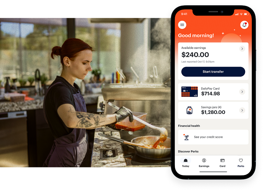 A person cooks in a kitchen while a smartphone screen in the foreground displays a financial app with account balances and transfer options.