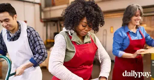 Three people in aprons work together, packing items in a warehouse.